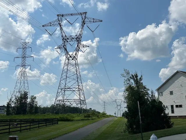 Large high-voltage lattice transmission towers running directly past a house and yard.