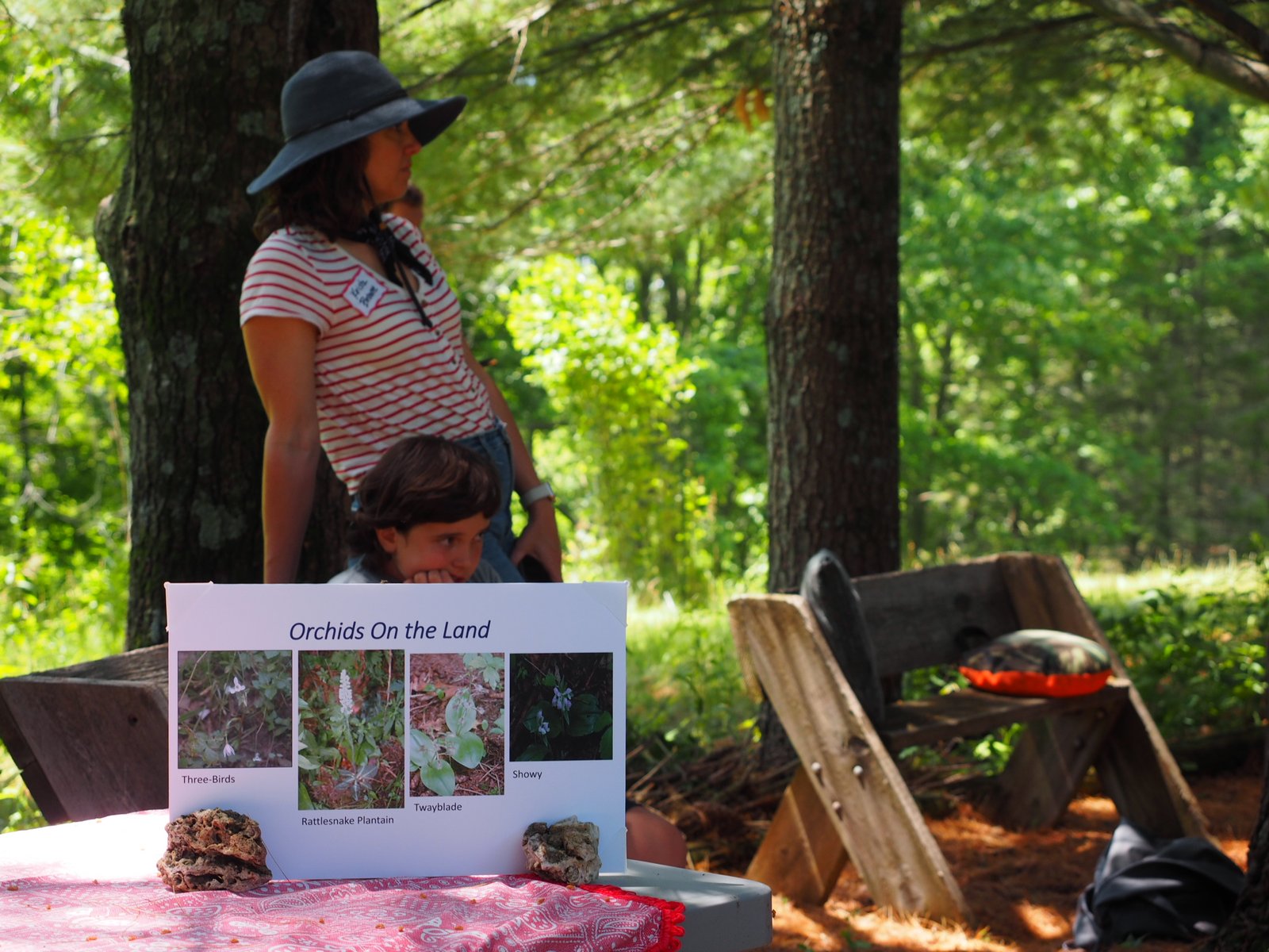 A woman stands beside an informational display titled 'Orchids on the Land' showing photographs of native orchid species.