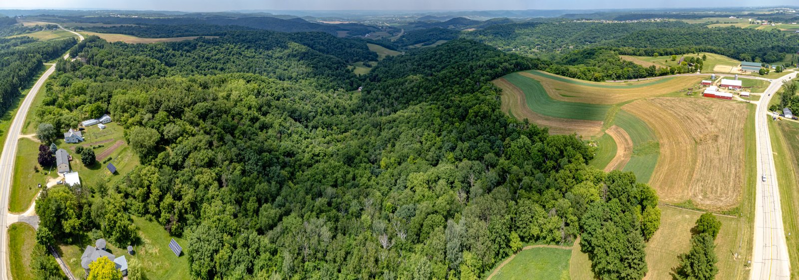 A wide overlook across the Driftless region of southwestern Wisconsin: forested rolling hills, farmed valleys, and ridgelines under a bright sky.