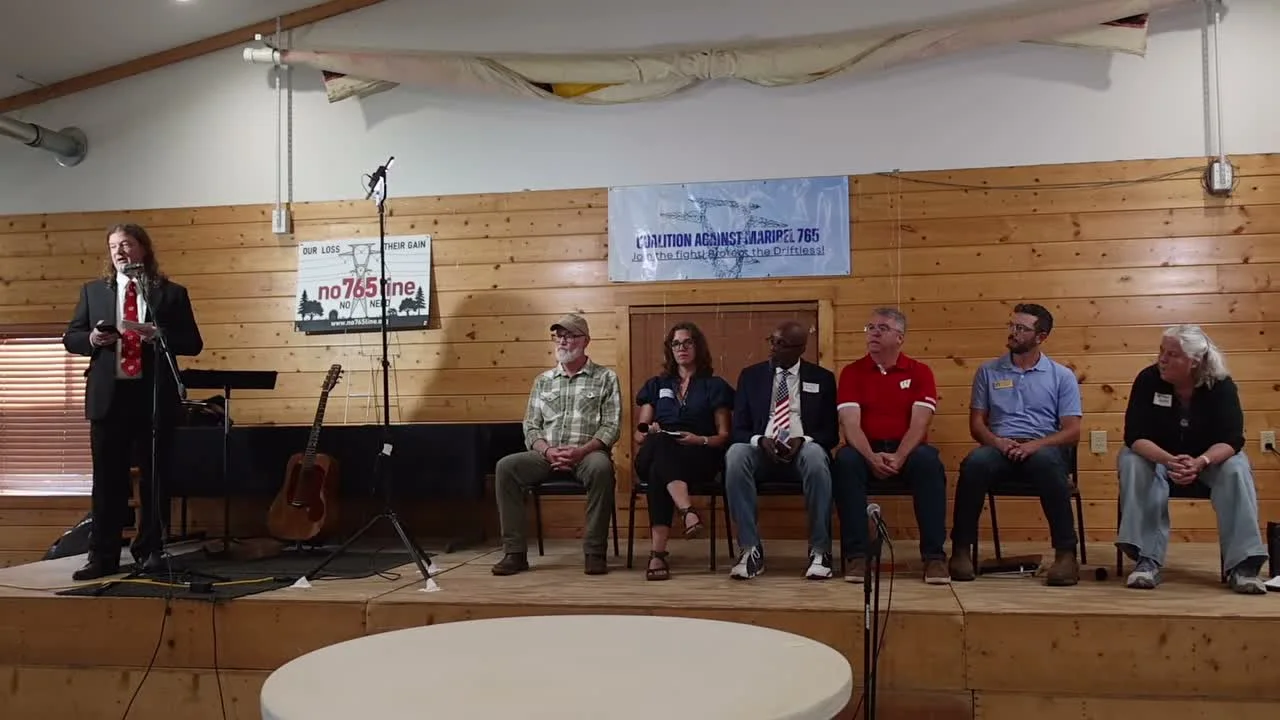 Moderator Erik Olsen speaks at a standing microphone beside a red No 765 Line sign reading Our Loss, Their Gain, while six panelists sit on a wooden stage beneath a Coalition Against Maribel 765 banner: Rep. Derrick Van Orden, Mayor Krista Browne, Dr. David D. King, Sen. Brad Pfaff, Rep. Travis Tranel, and Rep. Tara Johnson.