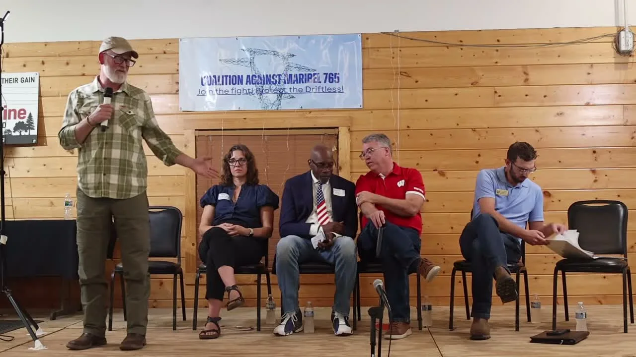 Rep. Derrick Van Orden, in a plaid shirt and ball cap, stands with a microphone and gestures while answering a question; Mayor Krista Browne, Dr. David D. King, Sen. Brad Pfaff, and Rep. Travis Tranel are seated behind him.