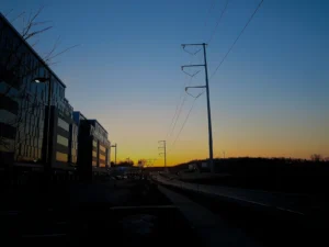 Steel monopoles carrying an American Transmission Co. 345 kV line, silhouetted against a dusk sky beside a road and office buildings in Madison, Wisconsin, March 2014.