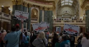 Residents hold up Our Loss, Their Gain, No 765 Line signs in the Wisconsin State Capitol Rotunda on October 13, 2026.