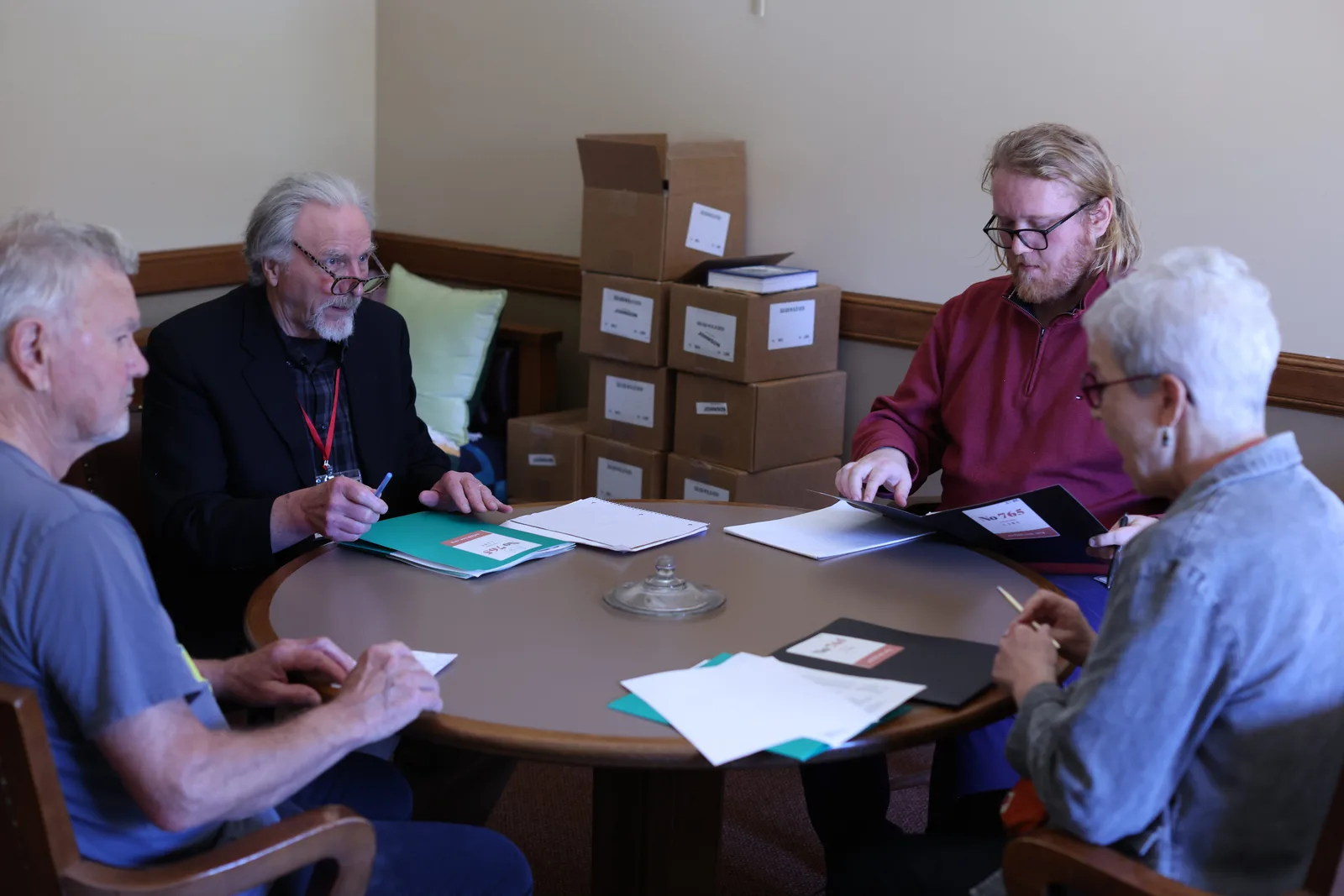 Photo 18 of 34. Residents and staff around a round table covered with packets.