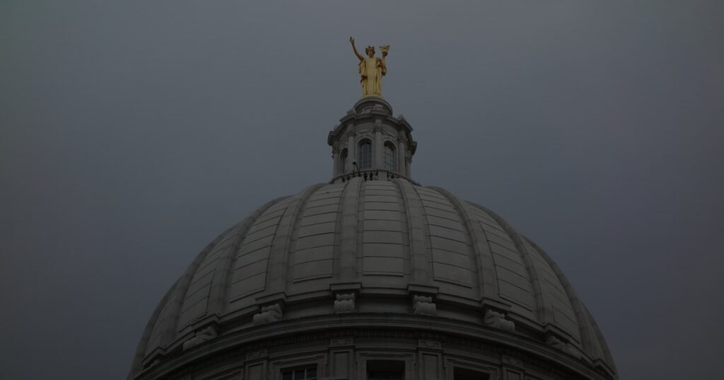 The dome of the Wisconsin State Capitol in Madison, with its gilded statue, against a gray sky.